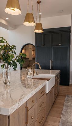 a large kitchen with marble counter tops and gold pendant lights hanging from the ceiling over the sink