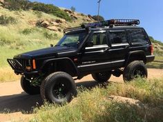 a black jeep parked on the side of a dirt road in front of a hill