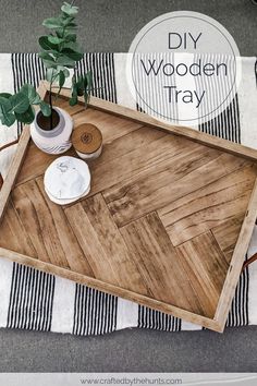 a wooden tray sitting on top of a striped blanket next to a potted plant