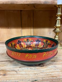 a red and green bowl sitting on top of a wooden table next to a candle