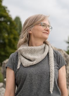 a woman wearing glasses and a scarf standing in front of rocks with trees behind her