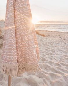 an umbrella on the beach with the sun peeking through it's fringed fabric