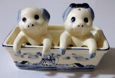 two ceramic figurines are sitting in a blue and white boat shaped container with the faces of two monkeys