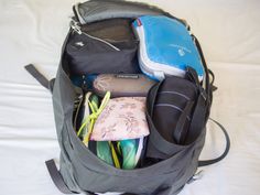 an open backpack filled with items on top of a bed