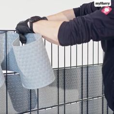 a man is holding two cups in front of a cage that has mesh material on it