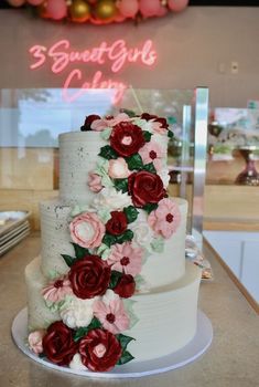 a three tiered wedding cake with red and pink flowers on it's side