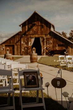 two white chairs sitting next to each other in front of a barn with an empty picture frame