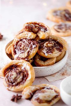 several cinnamon rolls in a white bowl on a table next to some other desserts