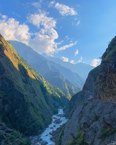 a river flowing through a valley surrounded by mountains under a blue sky with white clouds