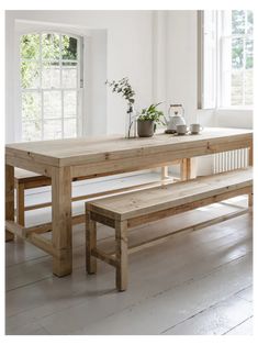 a wooden table and bench in a white room with windows on the far wall, potted plant next to it