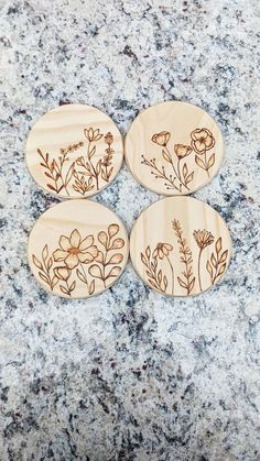 four wooden coasters with flowers on them sitting on a granite countertop in front of a marble background