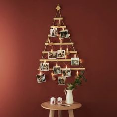 a wooden christmas tree with pictures hanging from it's sides and candles on the table