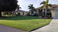 a large lawn in front of a house with palm trees on the side and two garages behind it