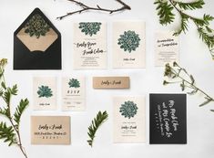 the wedding stationery is laid out on top of each other, with greenery and black envelopes