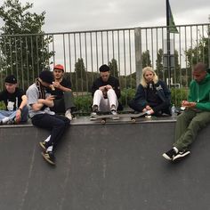 skateboarders are sitting on the edge of a ramp and looking at their phones