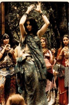 a group of women standing around each other in front of some trees and one woman is holding her hands up