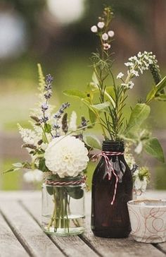 two mason jars with flowers in them sitting on a wooden table next to each other