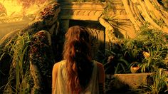 a woman with long hair standing in front of plants