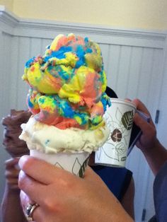 a person holding an ice cream cone with sprinkles on it and a cup in their hand