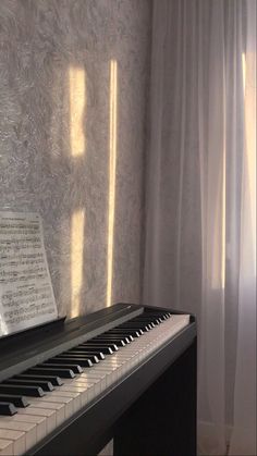 a piano sitting in front of a window next to a white curtain and sheeted wall