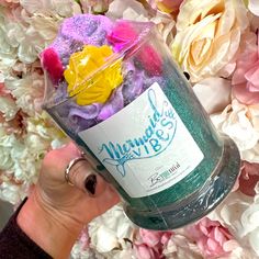 a person holding up a jar filled with soapy water surrounded by pink and yellow flowers