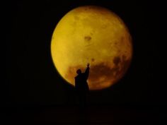 a person standing in front of a full moon with their hand up to the sky