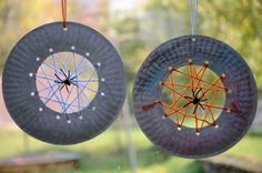 two circular objects hanging from strings in front of a window with grass and trees behind them