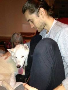 a man is petting a white dog while sitting on a bed with other people