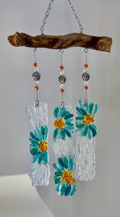 three pieces of glass with flowers hanging from chains on a tree branch and some beads attached to them