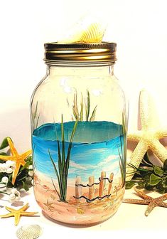 a glass jar filled with sand and sea grass on top of a white table next to starfish