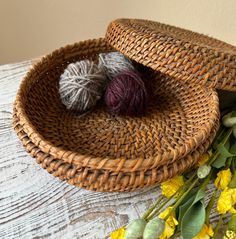 two balls of yarn sit in a woven basket next to flowers on a wooden table