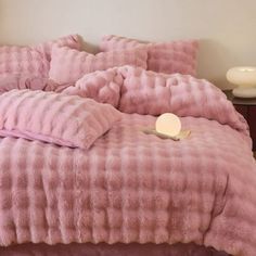 a bed with pink comforter and pillows on it in a white room next to a night stand