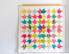 a multicolored quilt hanging on the wall next to a wooden frame with scissors