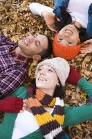 a man and woman laying in leaves with their heads on each other's shoulders