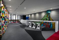 an office decorated with colorful tiles and white stools in front of a wall mural