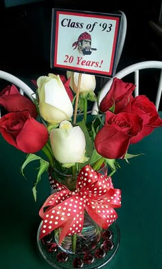 red and white roses in a clear vase with a bow on the top, next to a sign that says class of 1933