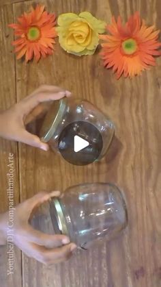 two hands are holding a mason jar with flowers on the table