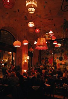 people sitting at tables in a restaurant with lights hanging from the ceiling