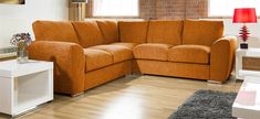 an orange sectional sofa in a living room with hardwood floors and brick wall behind it