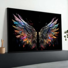 an artistic painting with colorful wings on a black wall next to a potted plant