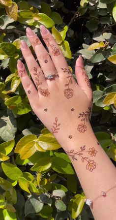 a woman's hand with tattoos on it and some leaves around her wrist, in front of bushes