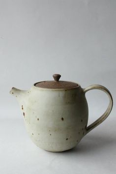 a white teapot with brown speckles sits on a plain surface, ready to be used as a coffee pot