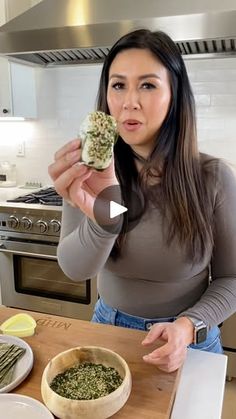 a woman holding up a piece of food in front of her face while sitting at a kitchen counter