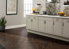 a kitchen with white cabinets and wood flooring next to a potted plant on the counter