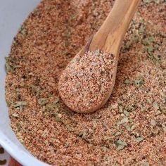 a wooden spoon in a white bowl filled with ground spices and seasoning flakes