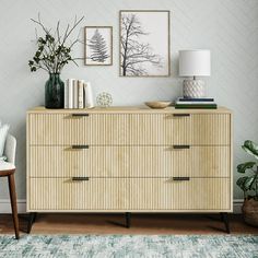 a living room with a dresser, chair and pictures on the wall above it that has plants in vases