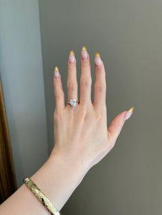 a woman's hand with gold and white manicures holding a diamond ring