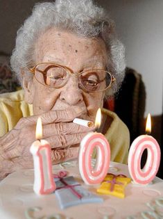 an old woman blowing out candles on her birthday cake with the number 100 written in it