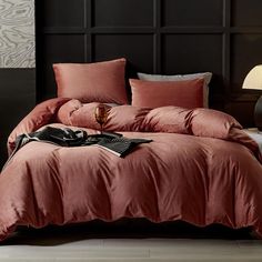 a bed with pink sheets and pillows in a room next to a night stand on the floor