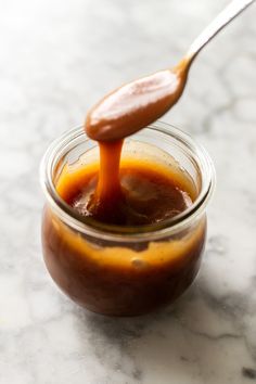 a spoon full of caramel sauce sitting on top of a jar filled with liquid